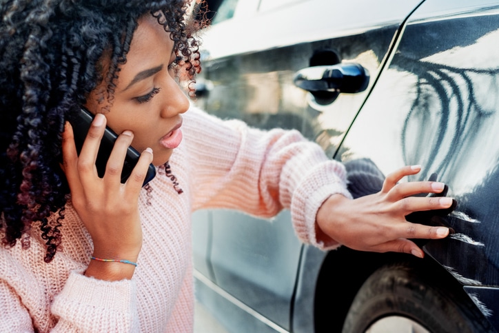 Woman on the phone examining car damage